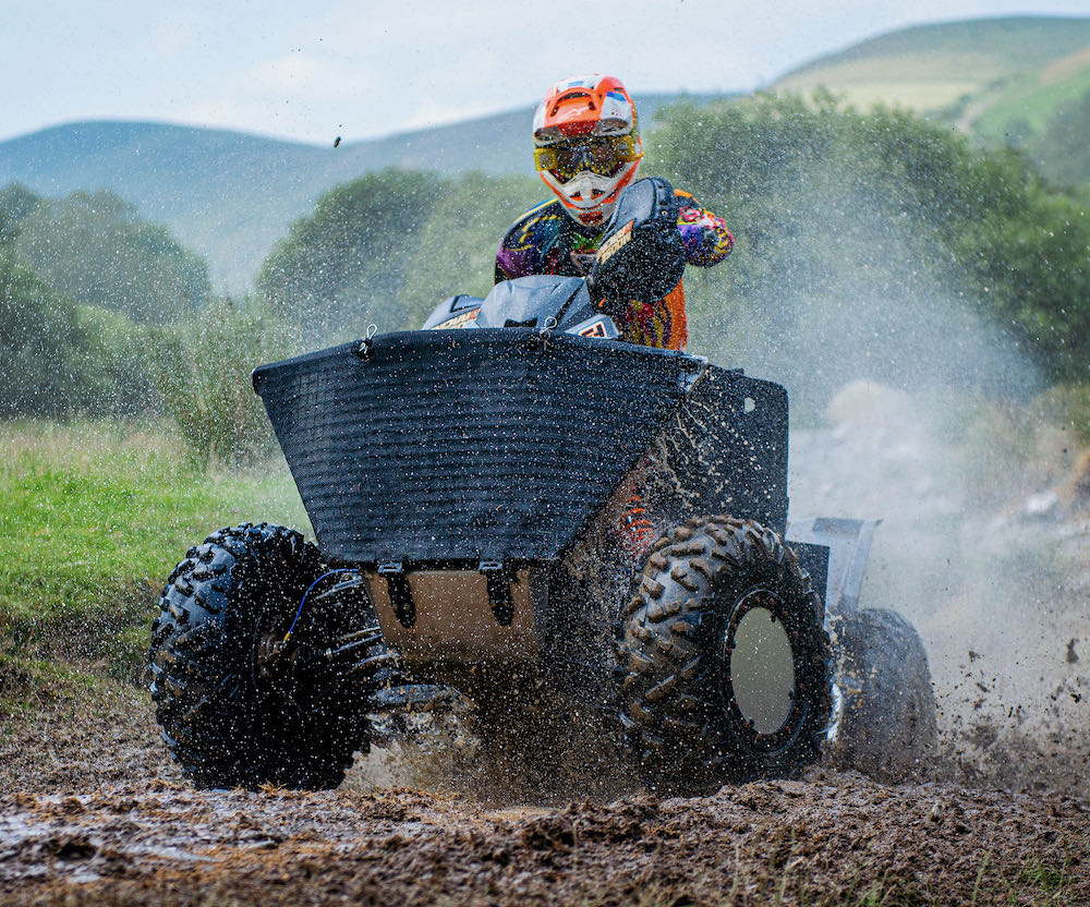 A person races an ATV through the muddy terrain of Wales, with hills and trees providing a scenic weekend backdrop.