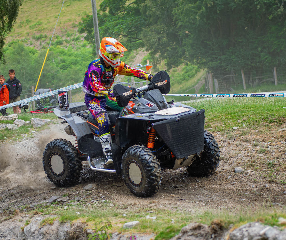 A person wearing colorful gear rides an ATV off-road on a rocky trail during a weekend adventure in Wales, with trees in the background.