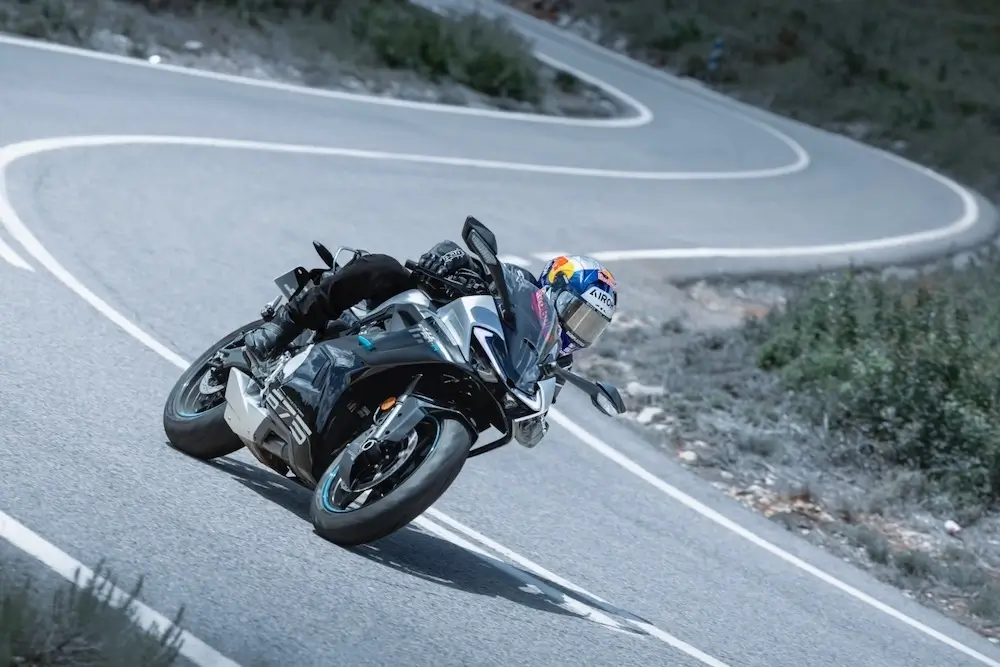 A motorcyclist wearing protective gear leans into a curve while riding a sport bike equipped with a CFMOTO T-Box on a winding mountain road.