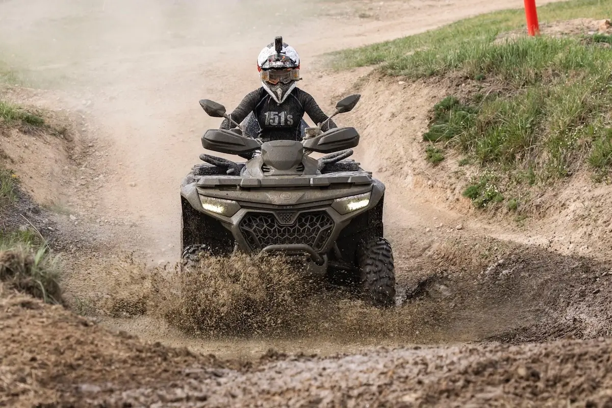 A person wearing a helmet with a camera rides a CForce 850 Touring ATV through a muddy puddle on a dirt trail.