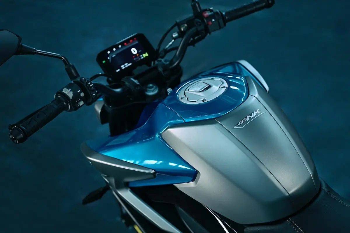 Close-up view of a blue and silver 125NK motorcycle's fuel tank, handlebars, and digital display, with the brand name "ZANK" visible on the tank.