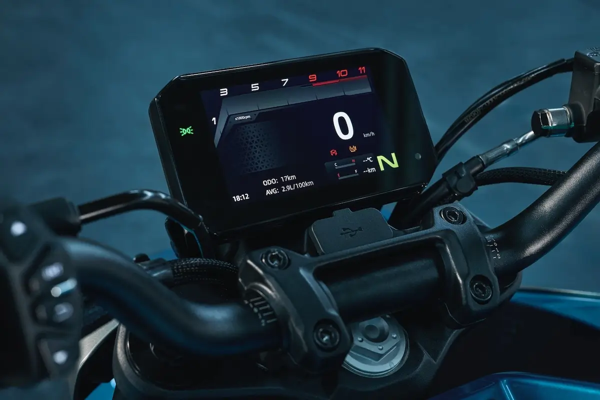 Close-up of a 125NK motorcycle digital dashboard displaying speed, gear position, RPM, and various ride information, with handlebars visible in the foreground.
