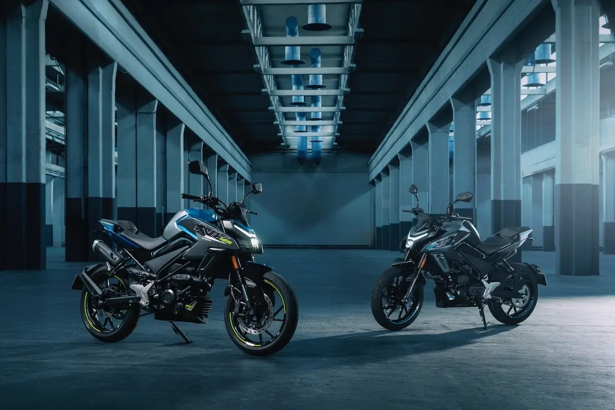 Two modern 125NK motorcycles are parked side by side in a spacious, industrial-style warehouse with tall columns and large windows.