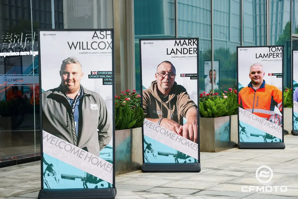 Three outdoor banners display portraits of men, each labeled with a name and the words "WELCOME HOME," in front of a modern glass building, highlighting the importance of ATV safety in their community.
