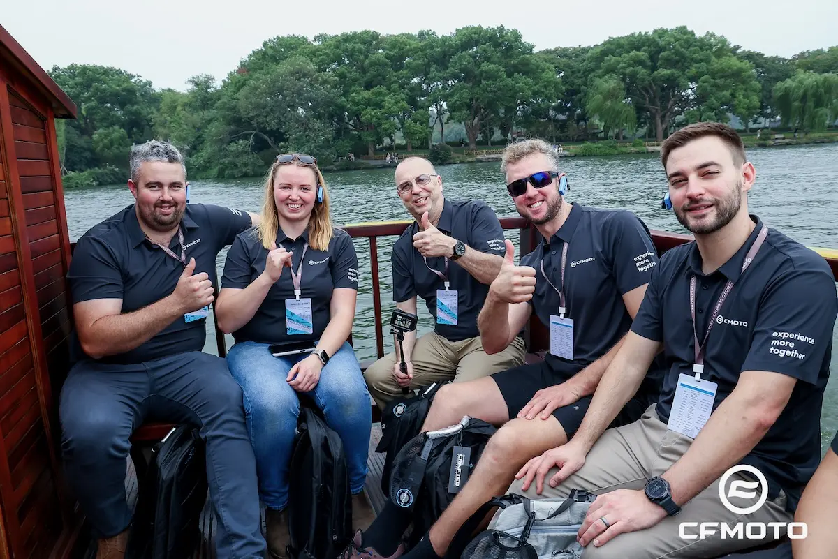 1M8A8472-opq4029243482 – Copy Five people in matching shirts sit on a boat, smiling and giving thumbs up. Trees and water are visible in the background. The image has a CFMOTO logo in the lower right corner, reflecting their commitment to fun and ATV safety.