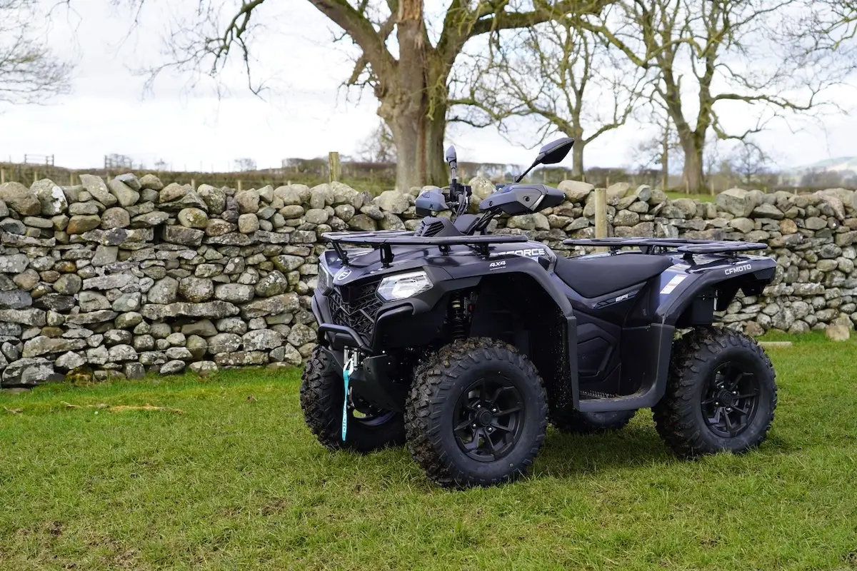 A black CForce 450 all-terrain vehicle (ATV) parked on grass in front of a stone wall and leafless trees.