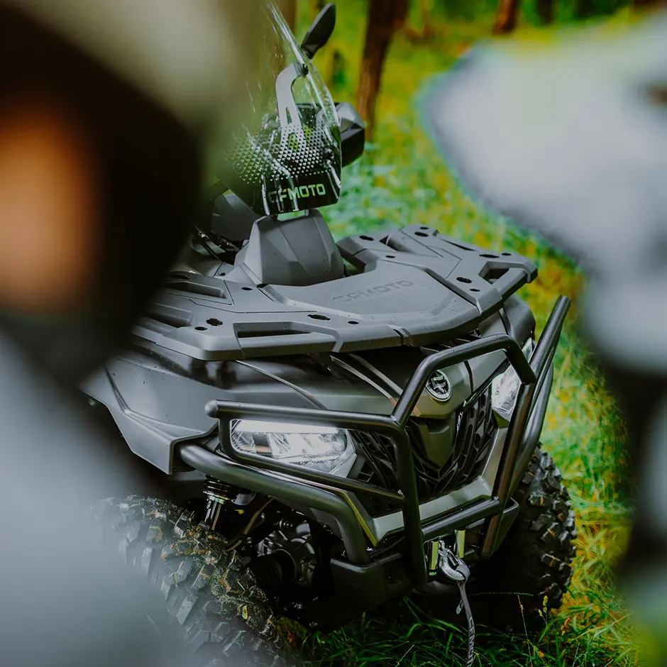Close-up of a black CFORCE 625 TOURING OVERLAND ATV parked on grass, highlighting the front grill, headlights, and rugged tires.