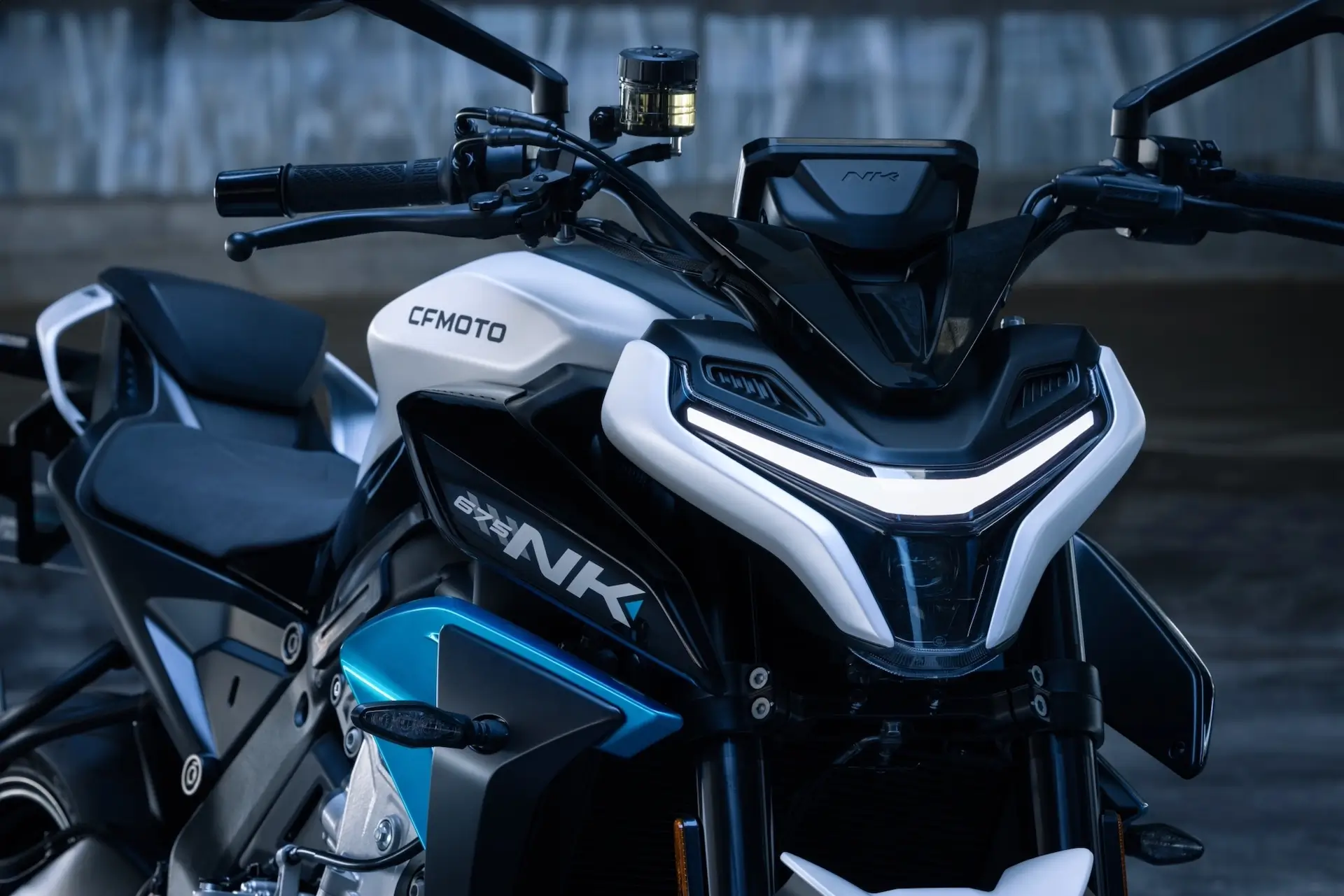 Close-up of the front and side view of a CFMOTO 800NK motorcycle, showcasing its handlebars, headlight, and part of the body with blue and white accents, alongside design cues reminiscent of the 125NK.