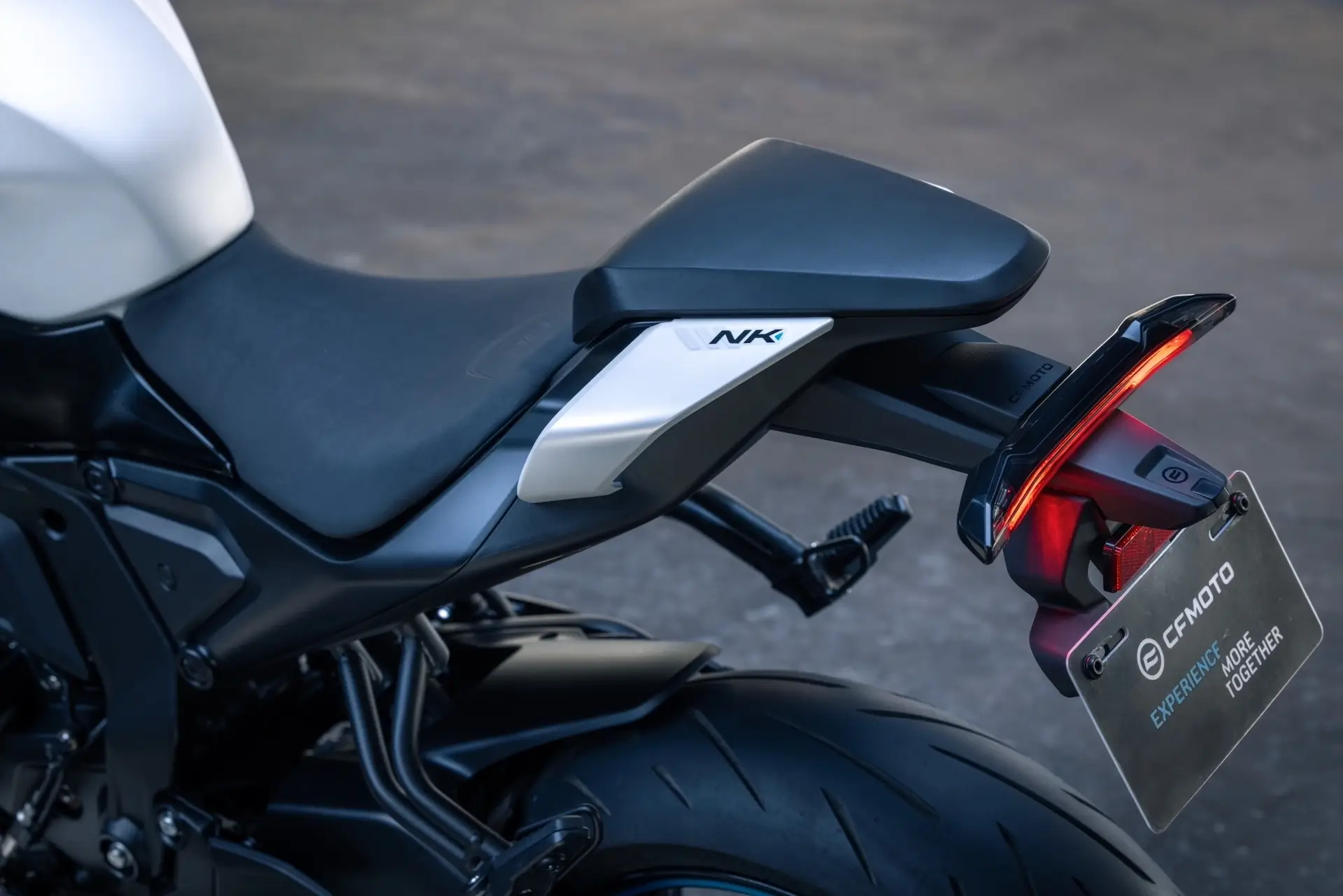 Close-up of the rear section of a black and white 125NK motorcycle, showing the seat, rear tire, tail light, and a license plate displaying the CFMOTO logo.