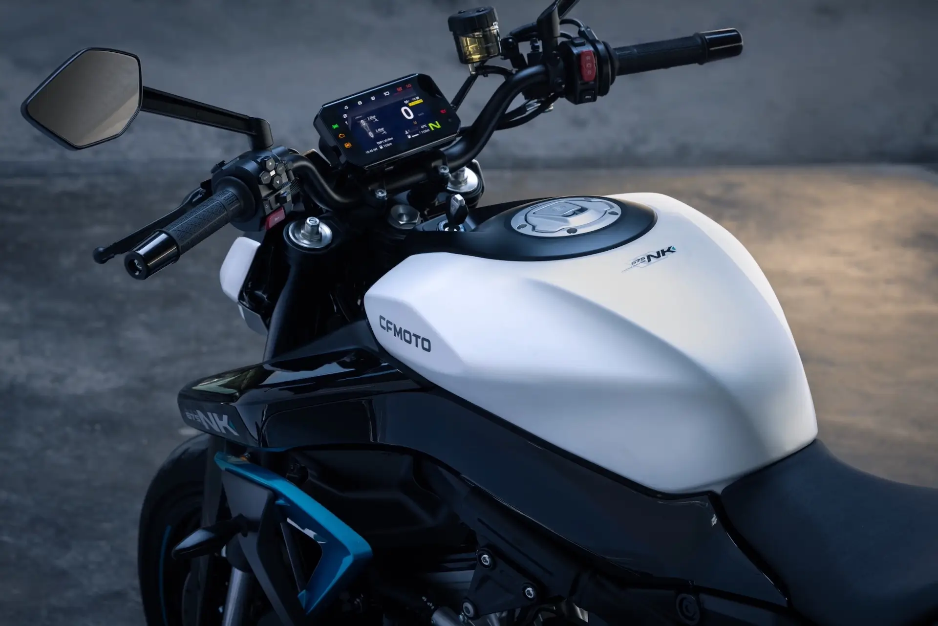 Close-up view of a CFMOTO 125NK motorcycle dashboard, handlebars, and fuel tank with a digital display, set against a concrete background.