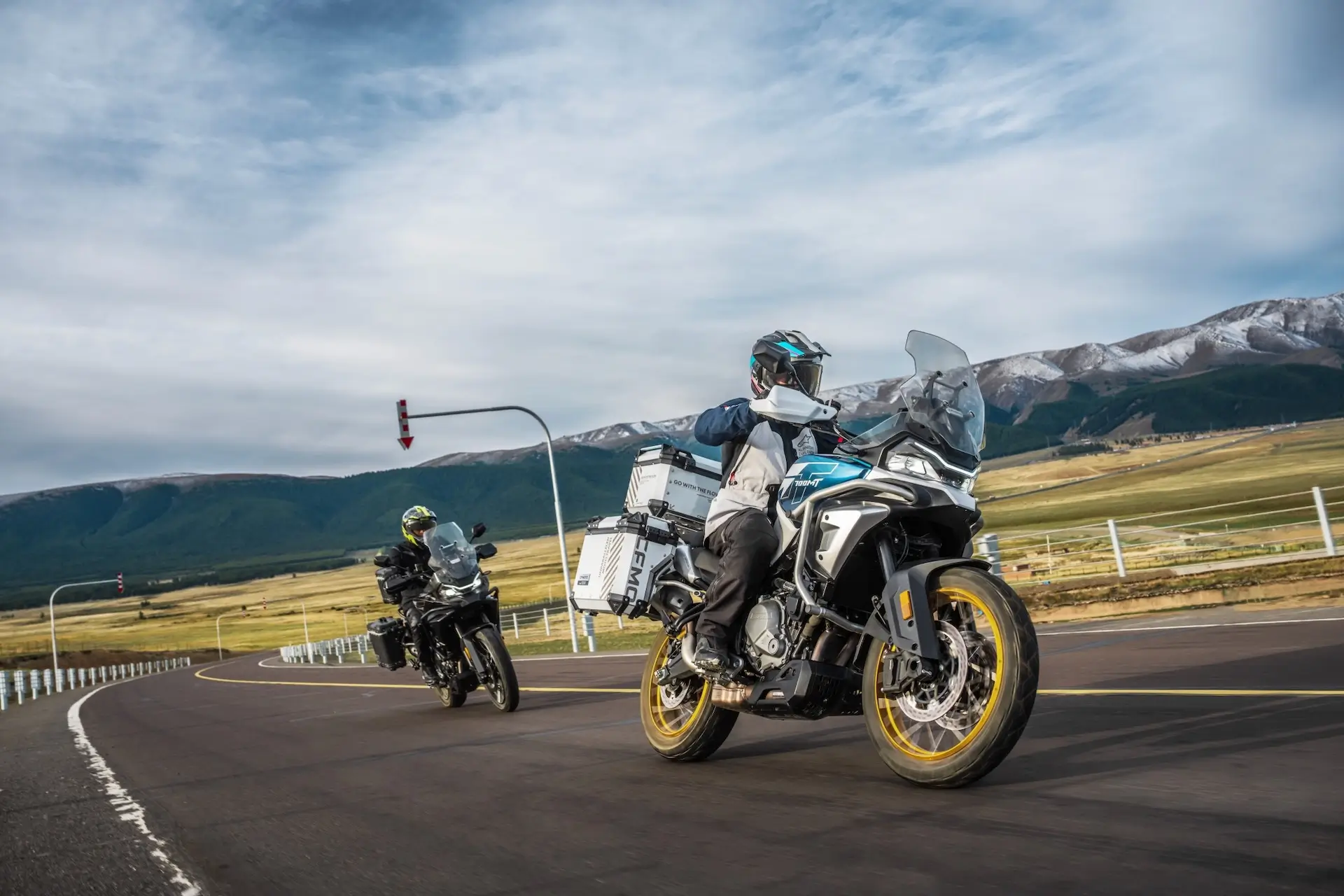 Two motorcyclists in protective gear ride 450MT adventure motorcycles on a winding road, surrounded by mountains and open fields.