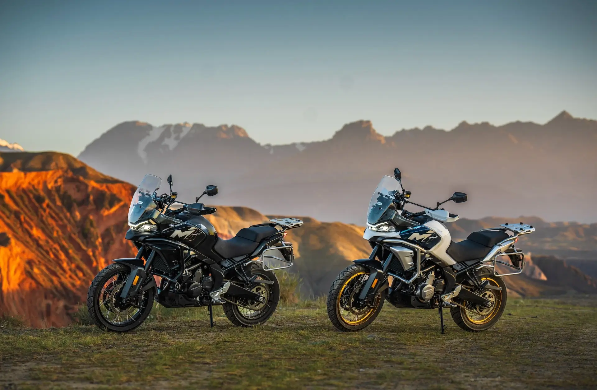 Two 450MT adventure motorcycles parked on grass with mountains and a colorful sunset sky in the background.