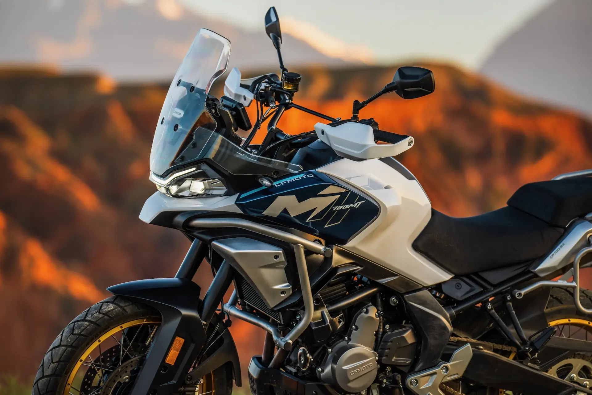 A white and black 450MT adventure motorcycle parked outdoors with rocky mountains in the background.