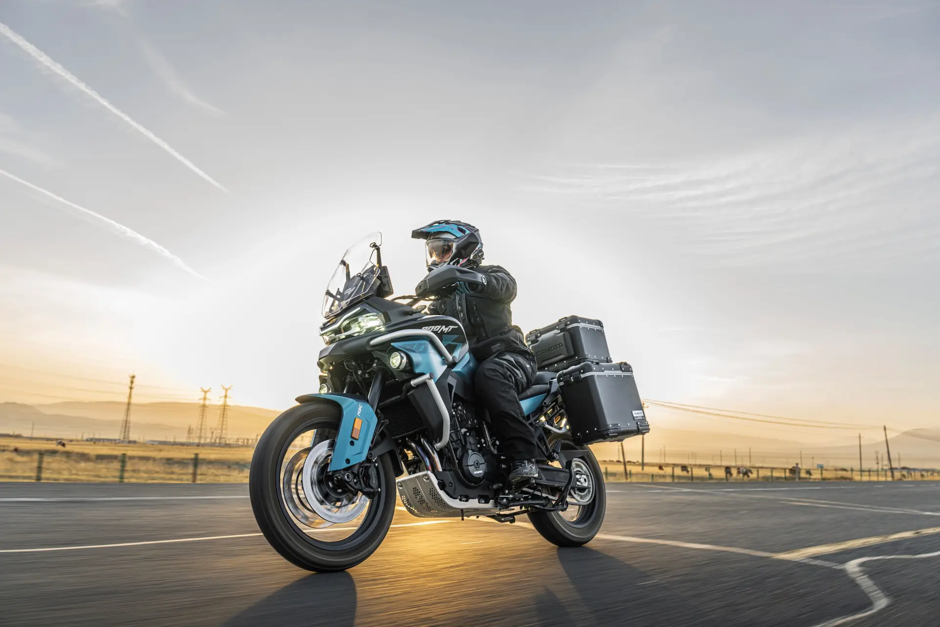 A person wearing a helmet rides an 800MT-X touring motorbike with panniers on an open road at sunrise or sunset.