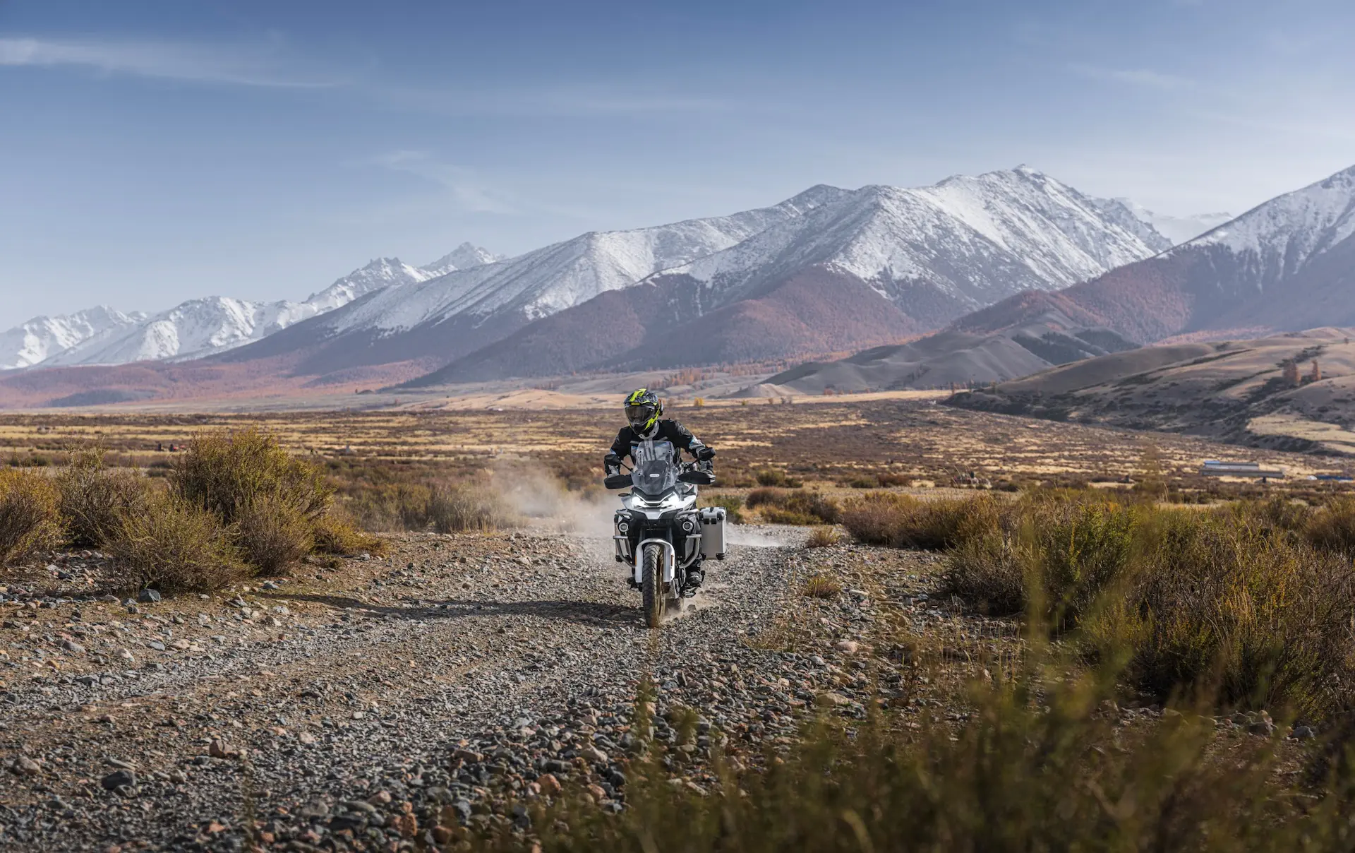 A person rides an 800MT-X motorbike on a rocky dirt road through a mountainous landscape with snow-capped peaks in the background.