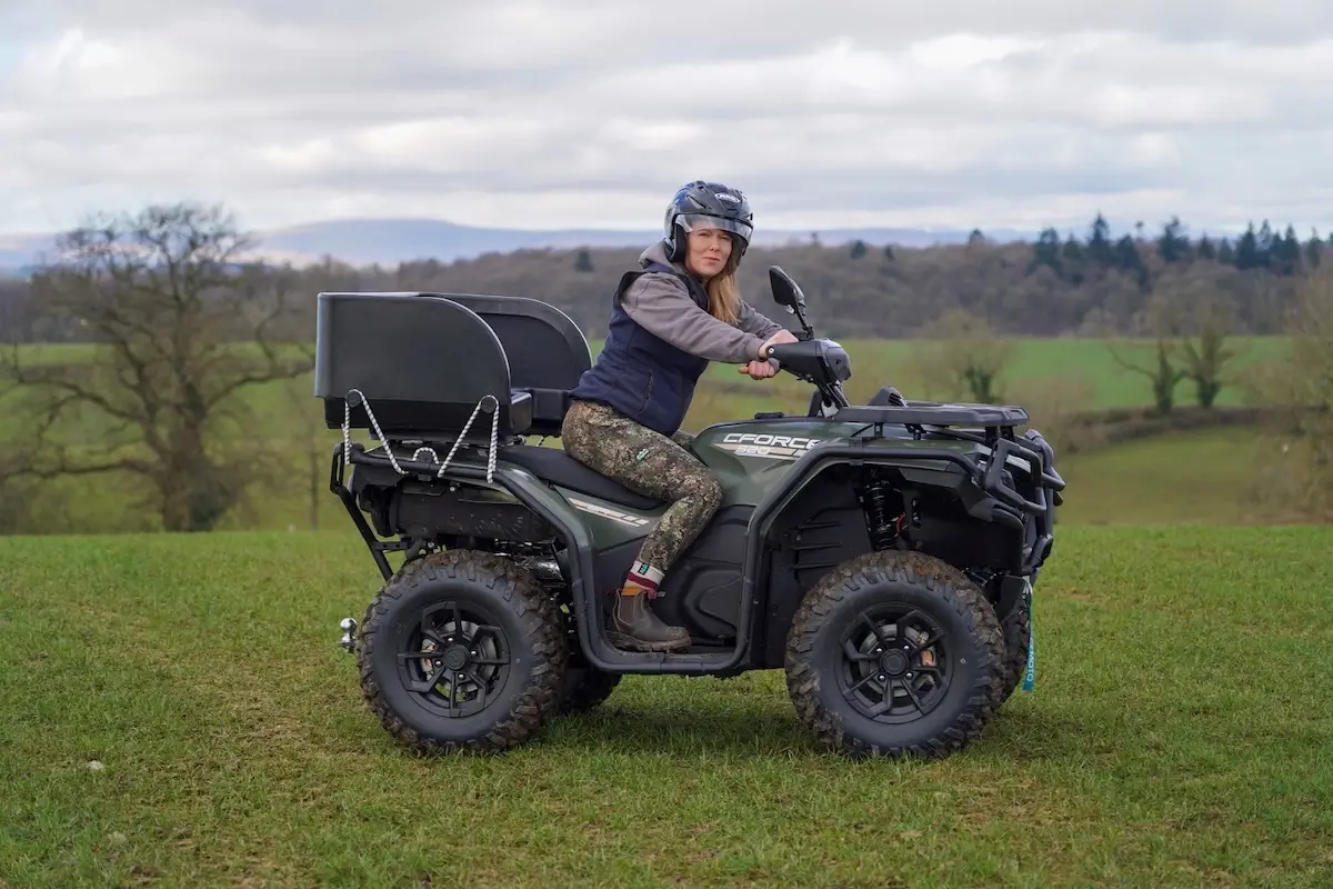 A person in a helmet and outdoor clothing sits on a black CForce 520 ATV in a grassy field, with trees and hills in the background.
