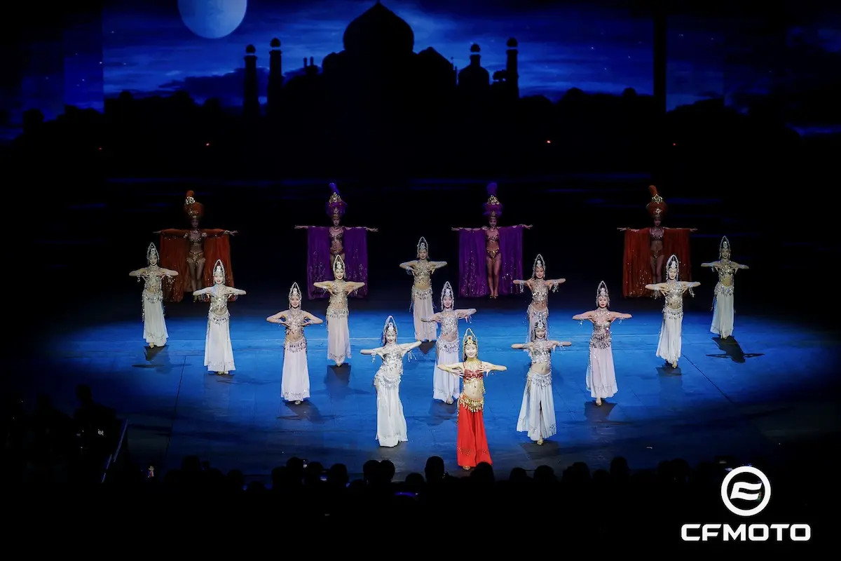 A group of dancers in ornate costumes perform on stage, framed by a night sky and architectural silhouette, with the CFMOTO logo in the corner—a nod to precision and the spirit of adventure inspired by ATV safety.