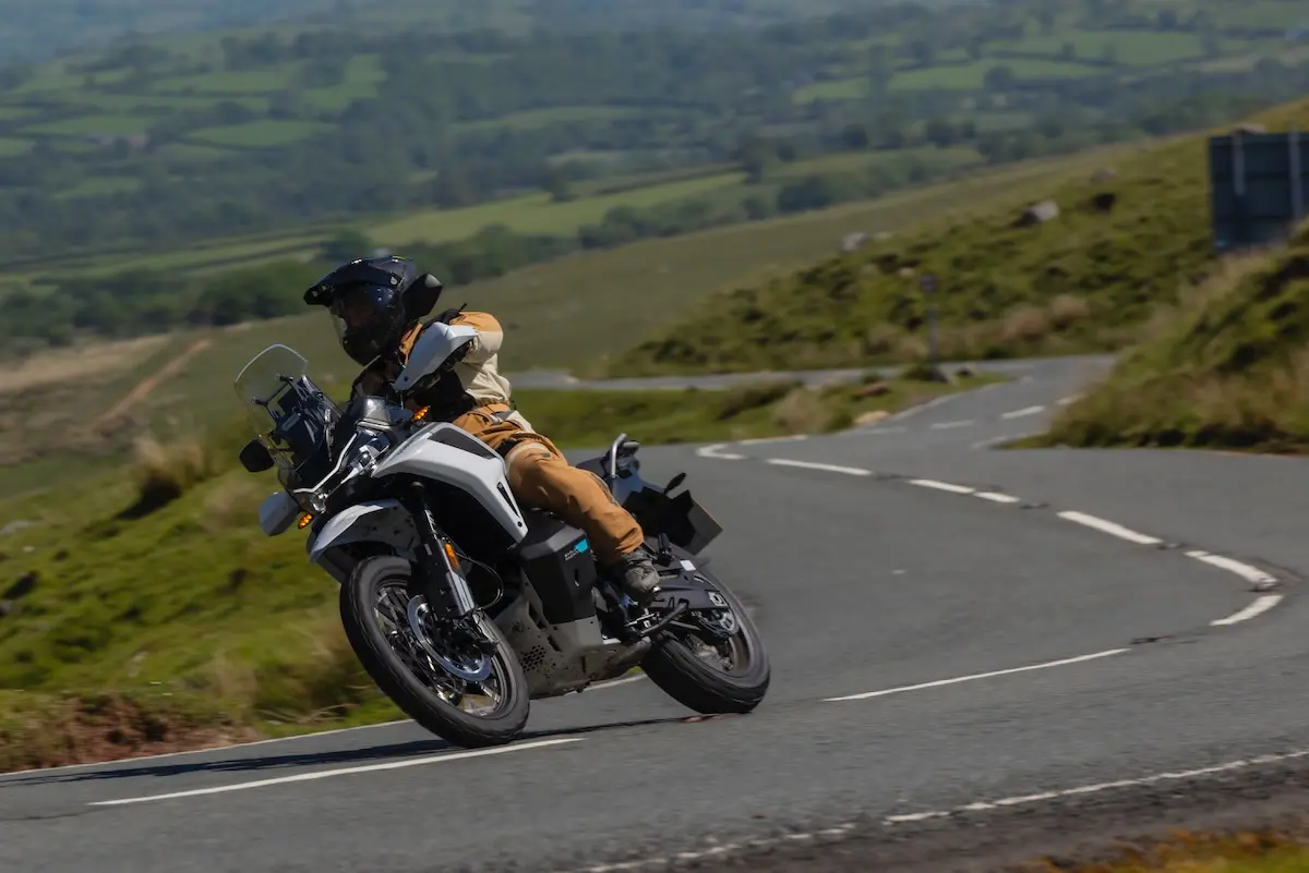 A person wearing protective gear rides a CFMOTO 1000MT-X round a bend on a rural road with green hills in the background, showcasing the bike's handling for this CFMOTO 1000MT-X review.