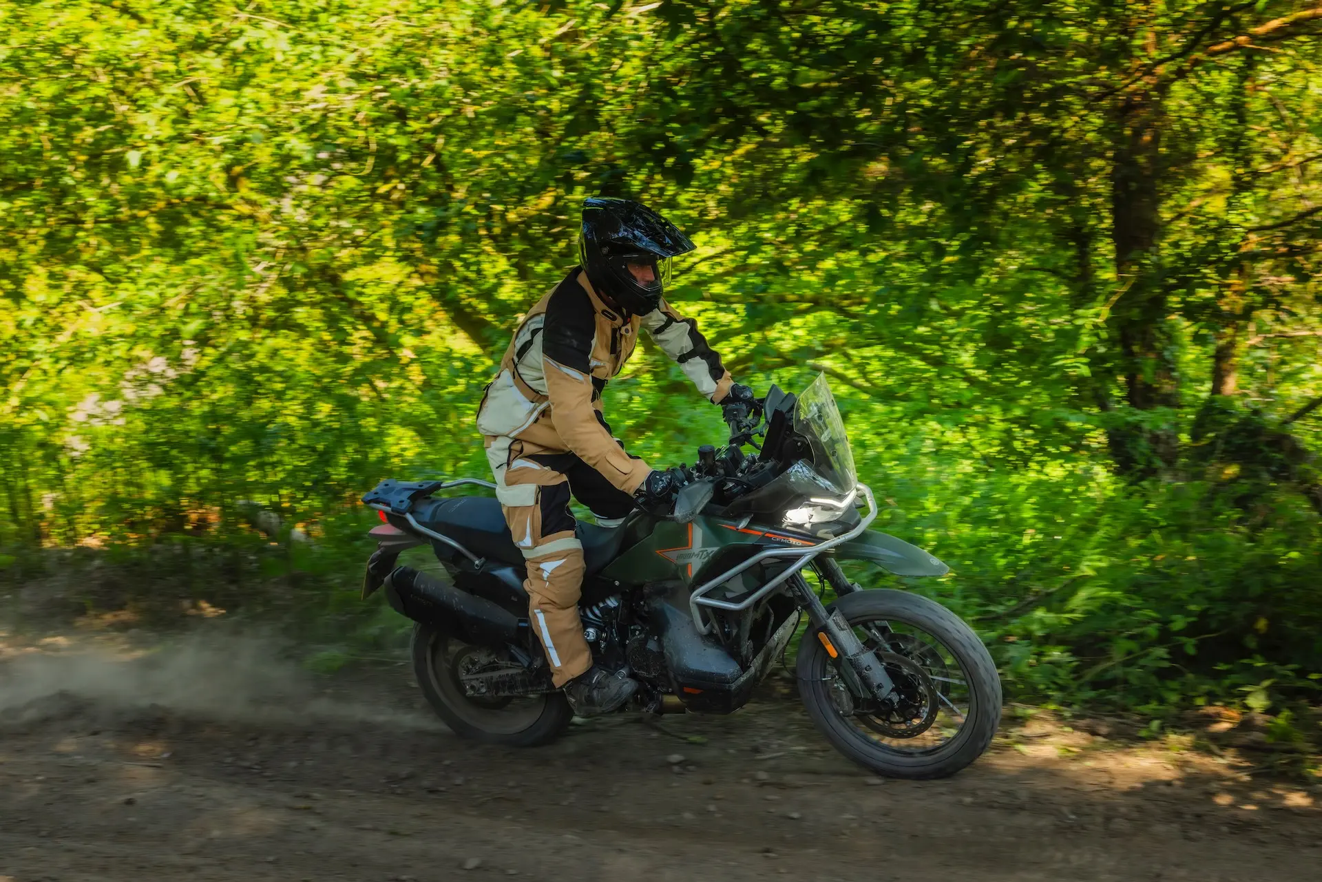 Person in protective gear riding a 1000MT-X motorbike on a dirt track through a lush green forest, kicking up dust behind the rear wheel.