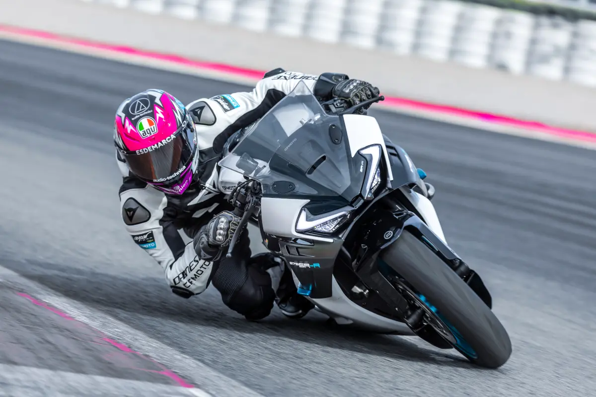 A motorcyclist in racing gear leans sharply into a turn on a CFMOTO sport motorbike with a Moto2 chassis maker on a racetrack.