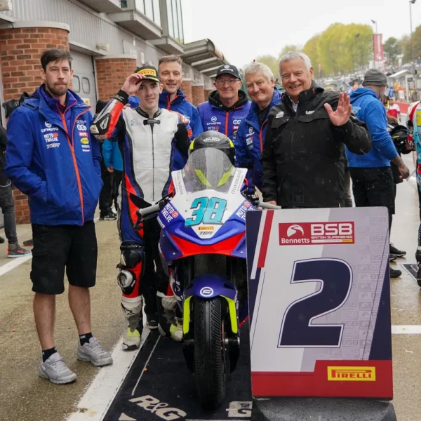 CFMOTO 675Sr-R racing 2 Six men pose next to a racing motorcycle and a sign showing the number 2 at a racetrack event. One man is in racing gear, while the others wear team uniforms, capturing the spirit of an exciting track day.