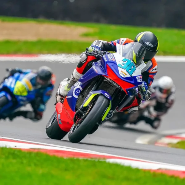 CFMOTO 675SR-R racing Three racing motorcycles lean into a curve on a track day, with the leading rider wearing number 38 and spraying liquid from the back of the bike.