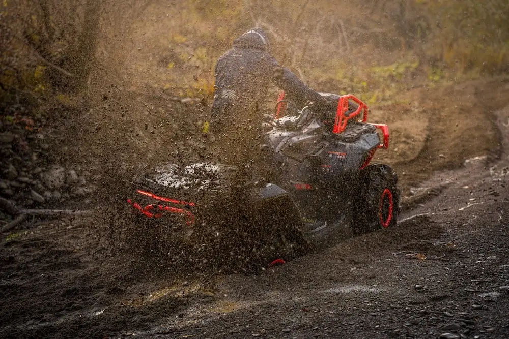 A person rides a UFORCE U10 XL PRO ATV through muddy terrain, with mud splashing up around the vehicle on a rough outdoor trail.