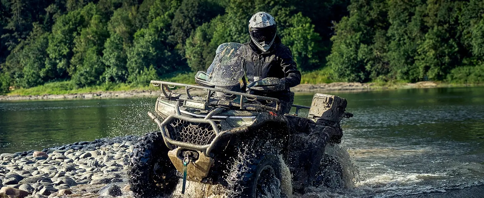 A person skillfully navigates a CFORCE 1000 Touring Premium through a shallow river, the ATV's robust power seamlessly blending with the serene forest backdrop.