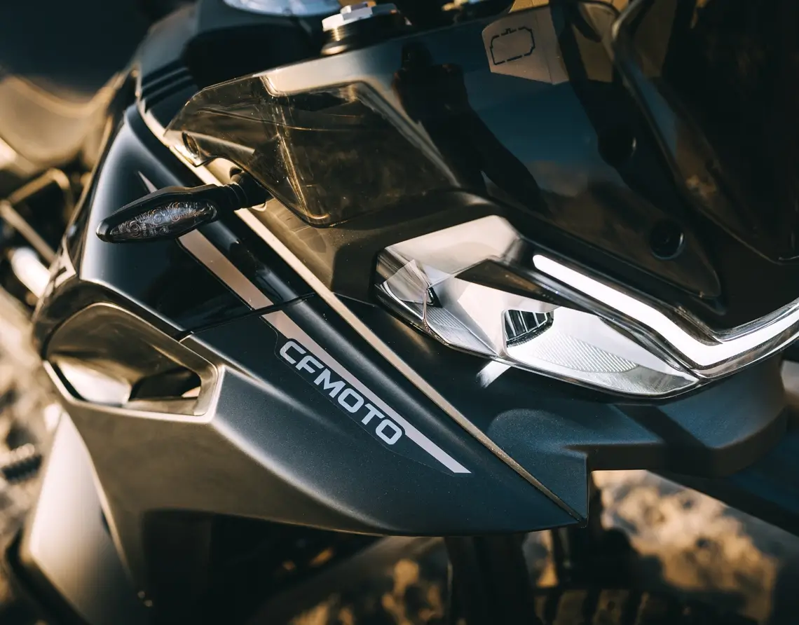 Close-up of the front section of a black CFMOTO 800MT-X motorcycle, showing the headlight, mirror, and part of the windshield.