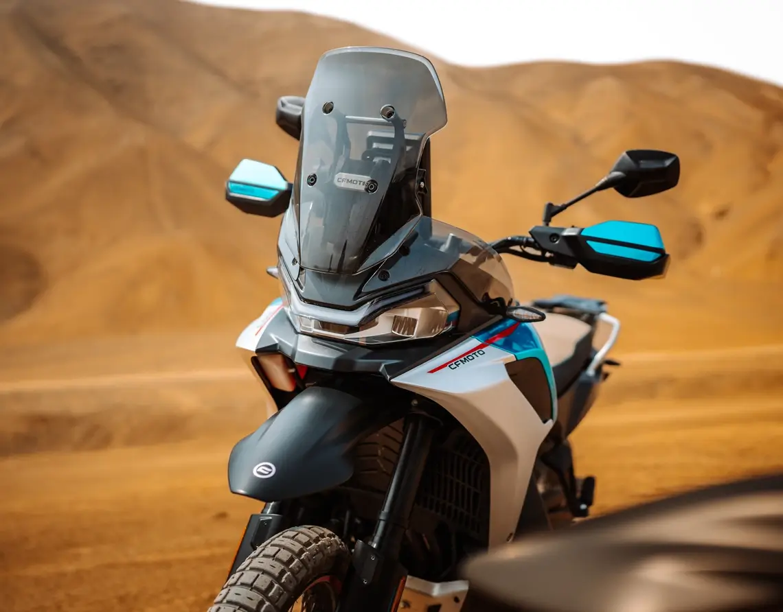 An 800MT-X dual-sport motorcycle with blue accents is parked on a dirt road in a desert landscape, framed by tan hills in the background.