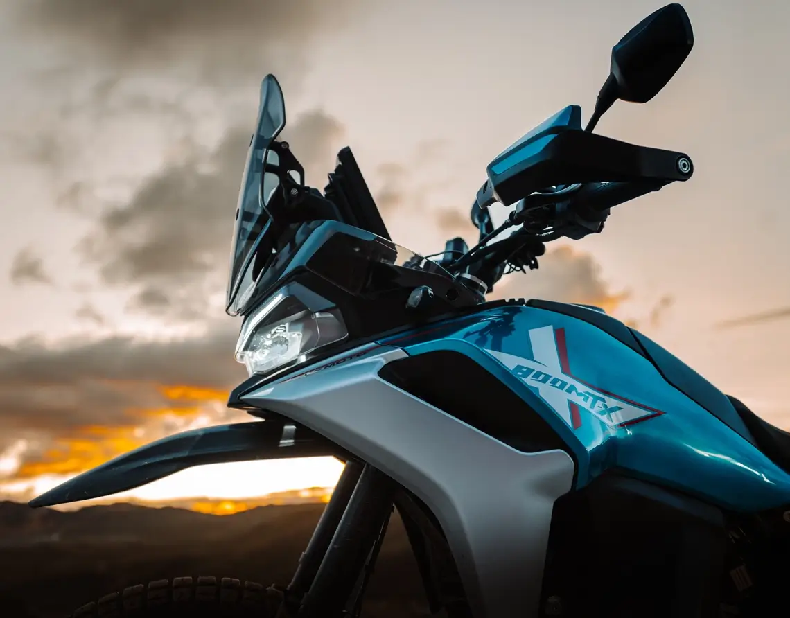 Close-up of a blue 800MT-X adventure motorcycle with a windshield and handguards, photographed outdoors at sunset with mountains in the background.