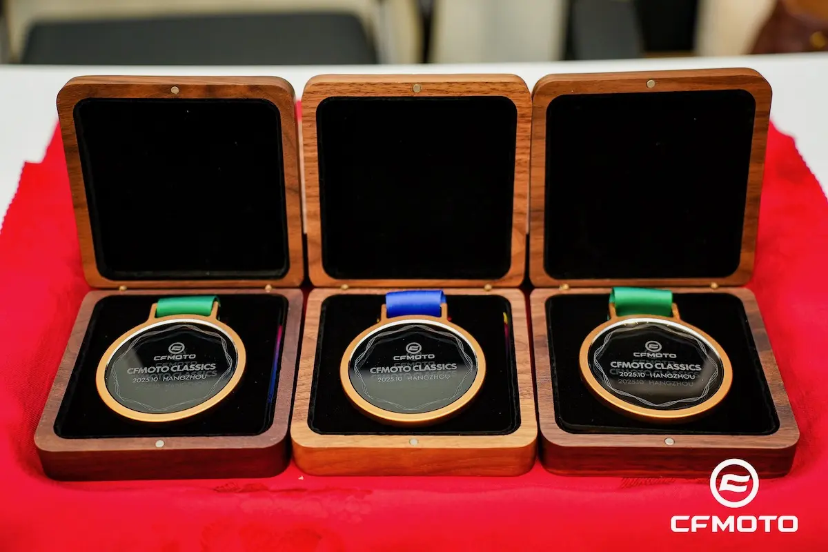 Three medals in wooden cases are displayed on a red cloth. Featuring the CFMOTO logo and "CFMOTO CLASSICS" text, these awards recognize excellence in ATV safety, each with a distinctively colored ribbon.