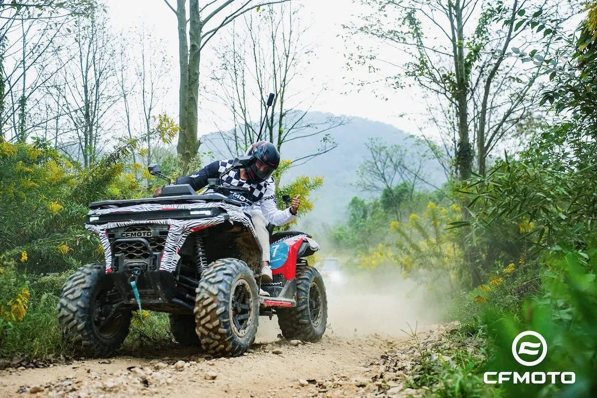 DSC02277-opq4030436584 A person practices ATV safety while riding a four-wheeler on a rocky dirt trail through a wooded area, raising dust, with the "CFMOTO" logo visible in the corner.