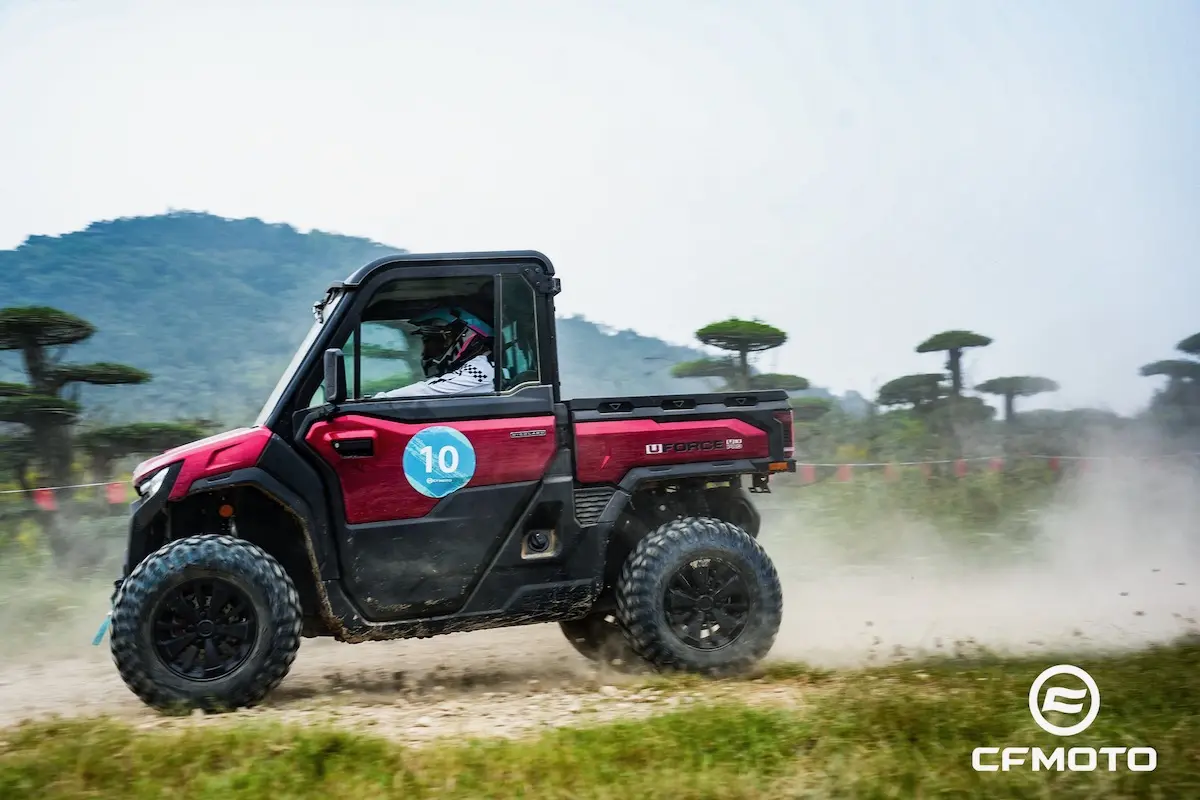 A red off-road utility vehicle displaying the number 10 on the door drives along a dirt path, raising dust and highlighting ATV safety, with trees and hills in the background. The CFMOTO logo is in the bottom right corner.