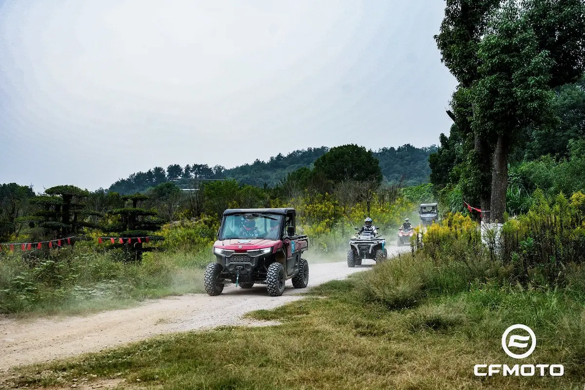 A group of off-road vehicles enjoys a dirt path through a green, rural landscape under a cloudy sky, showcasing the importance of ATV safety. The CFMOTO logo appears in the bottom right corner.