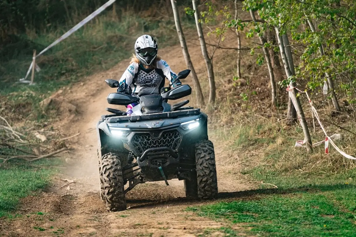 A person wearing a helmet and protective gear rides an ATV, one of the top estate management utility vehicles, along a dirt trail through a wooded area.