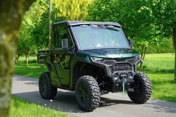 A green off-road utility vehicle, ideal for estate management, is parked on a paved path surrounded by lush green grass and trees.