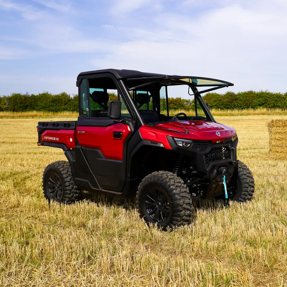 A red UFORCE U10 PRO HIGHLAND off-road utility vehicle is parked on a dry grassy field with hay bales and trees in the background under a partly cloudy sky.