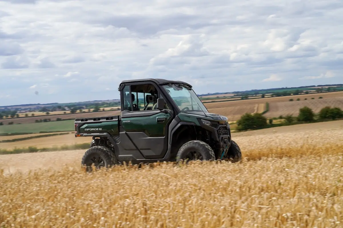 A dark green UFORCE U10 PRO HIGHLAND utility vehicle drives through a golden field with rolling farmland and a cloudy sky in the background.