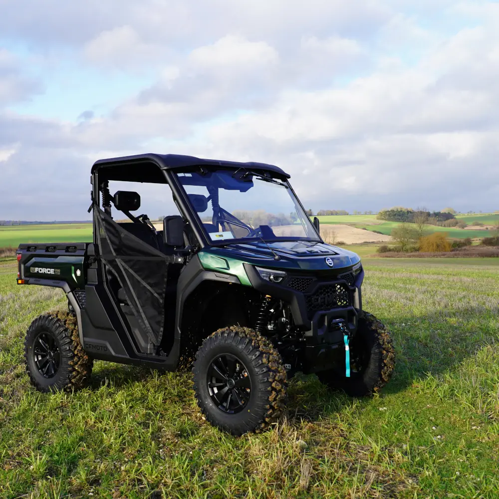 A black and green utility terrain vehicle (UTV) from the fleet is parked on a grassy field, set against rolling hills and a cloudy sky in the background.