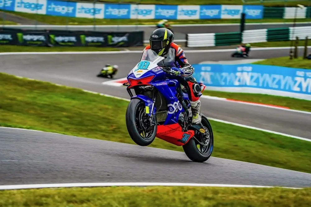 A motorcycle racer in full gear lifts the front wheel off the ground while speeding around a racetrack during a race, showcasing the dynamic power and control enabled by advanced tech like the CFMOTO T-Box.