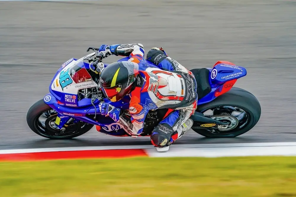 A motorcyclist in racing gear leans sharply into a turn on a racetrack while riding a blue and red sport bike equipped with the CFMOTO T-Box.