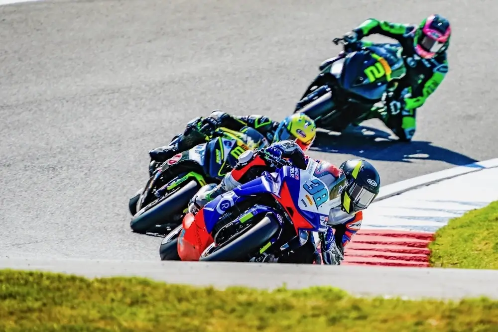 Four motorcycle racers lean into a turn on a racetrack, closely following each other in full racing gear and helmets, each bike equipped with advanced CFMOTO T-Box technology for real-time performance monitoring.