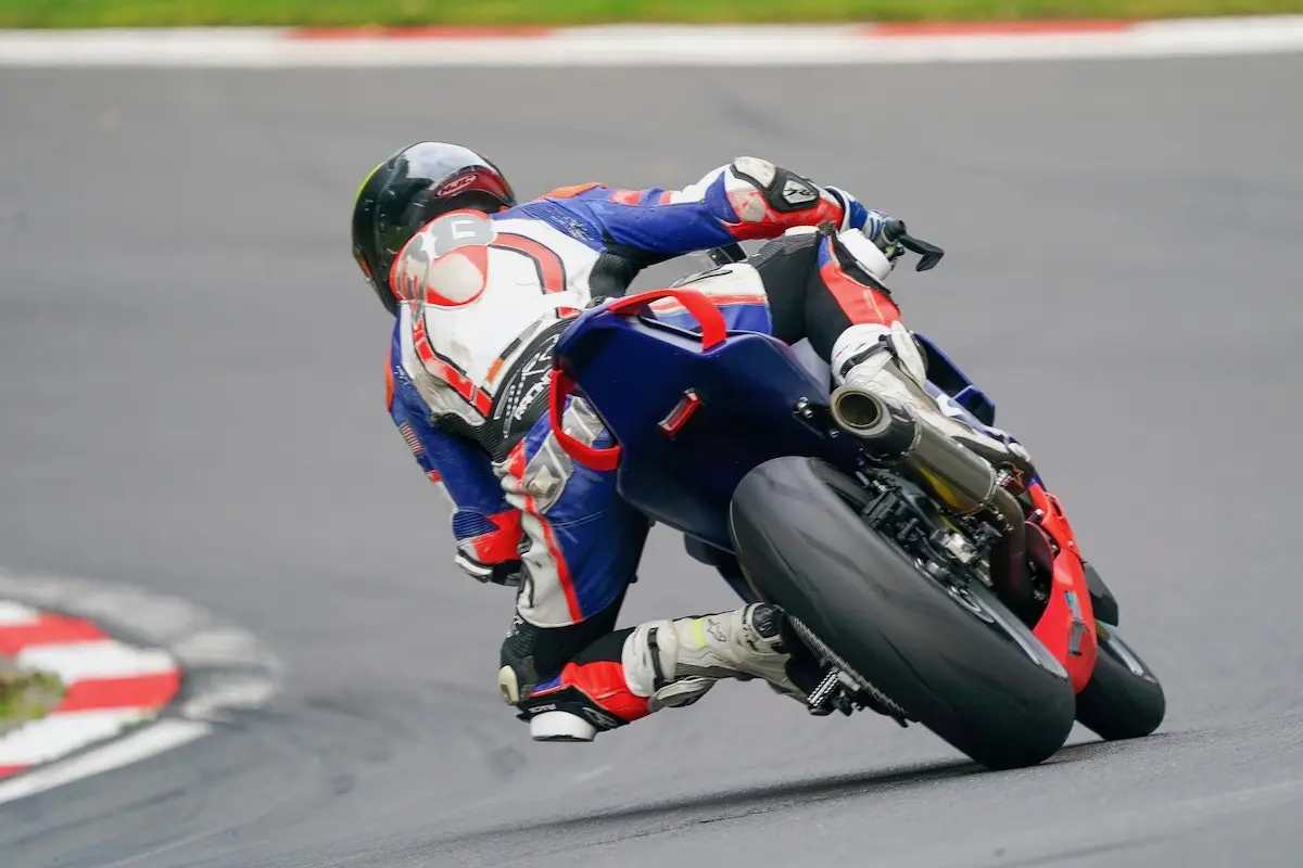A motorcycle racer in full gear, competing in the National Sportbike Podium, leans sharply into a racetrack curve, with the CFMOTO bike close to the ground and its tires gripping the asphalt.