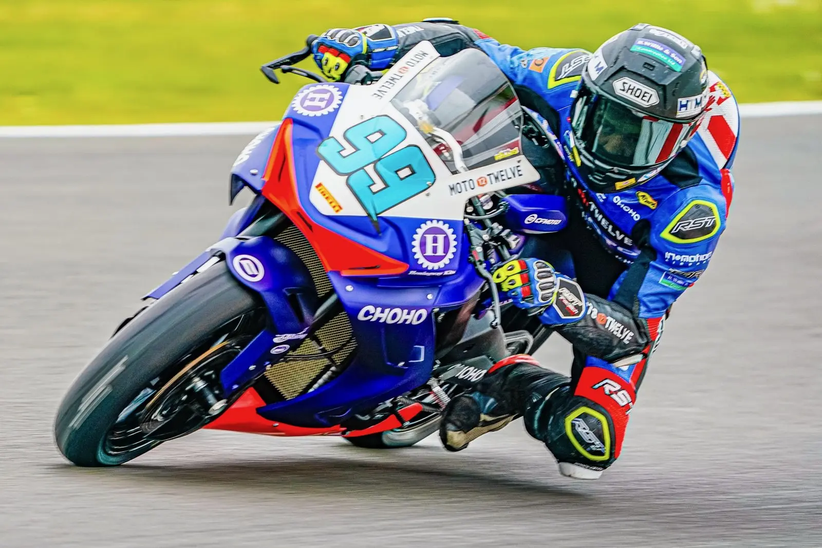 A motorcyclist in blue kit and helmet leans sharply into a bend at Oulton Park, riding a blue CFMOTO sportsbike marked with the number 99.
