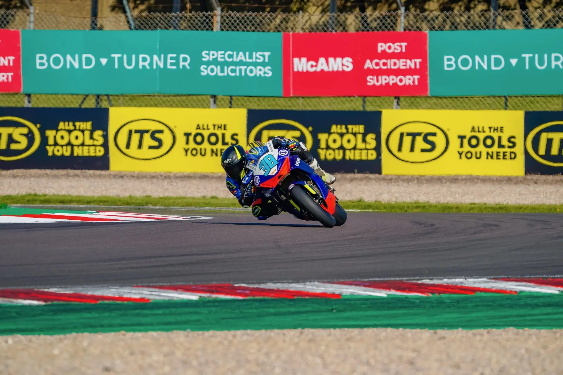 A motorcycle racer leans into a bend on the Donington Park racetrack, with CFMOTO advertising banners visible in the background.
