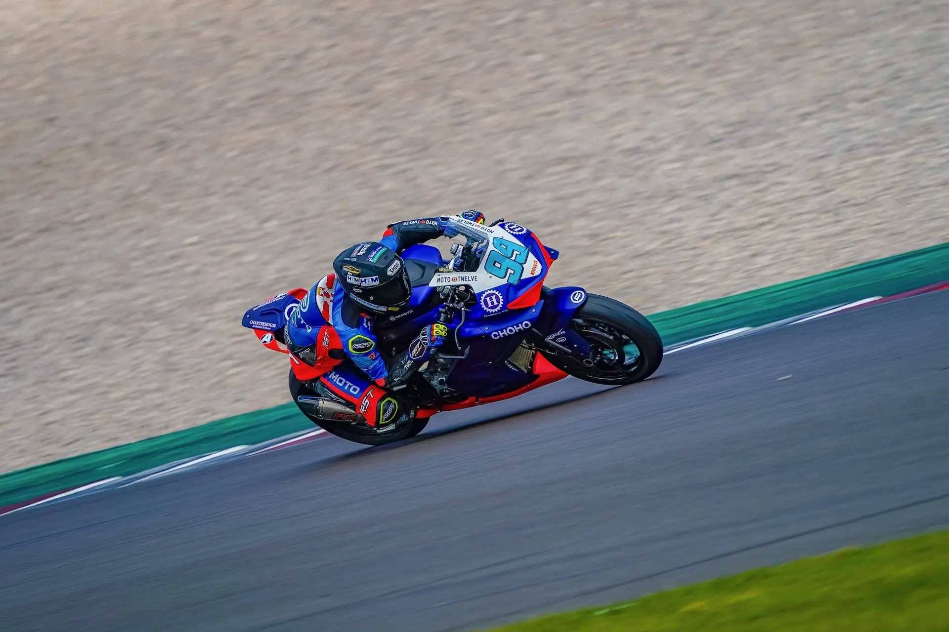 Motorcyclist wearing racing kit rides a blue and red CFMOTO sports bike on Donington Park’s tarmac racetrack, leaning into a bend during the Moto Twelve event.