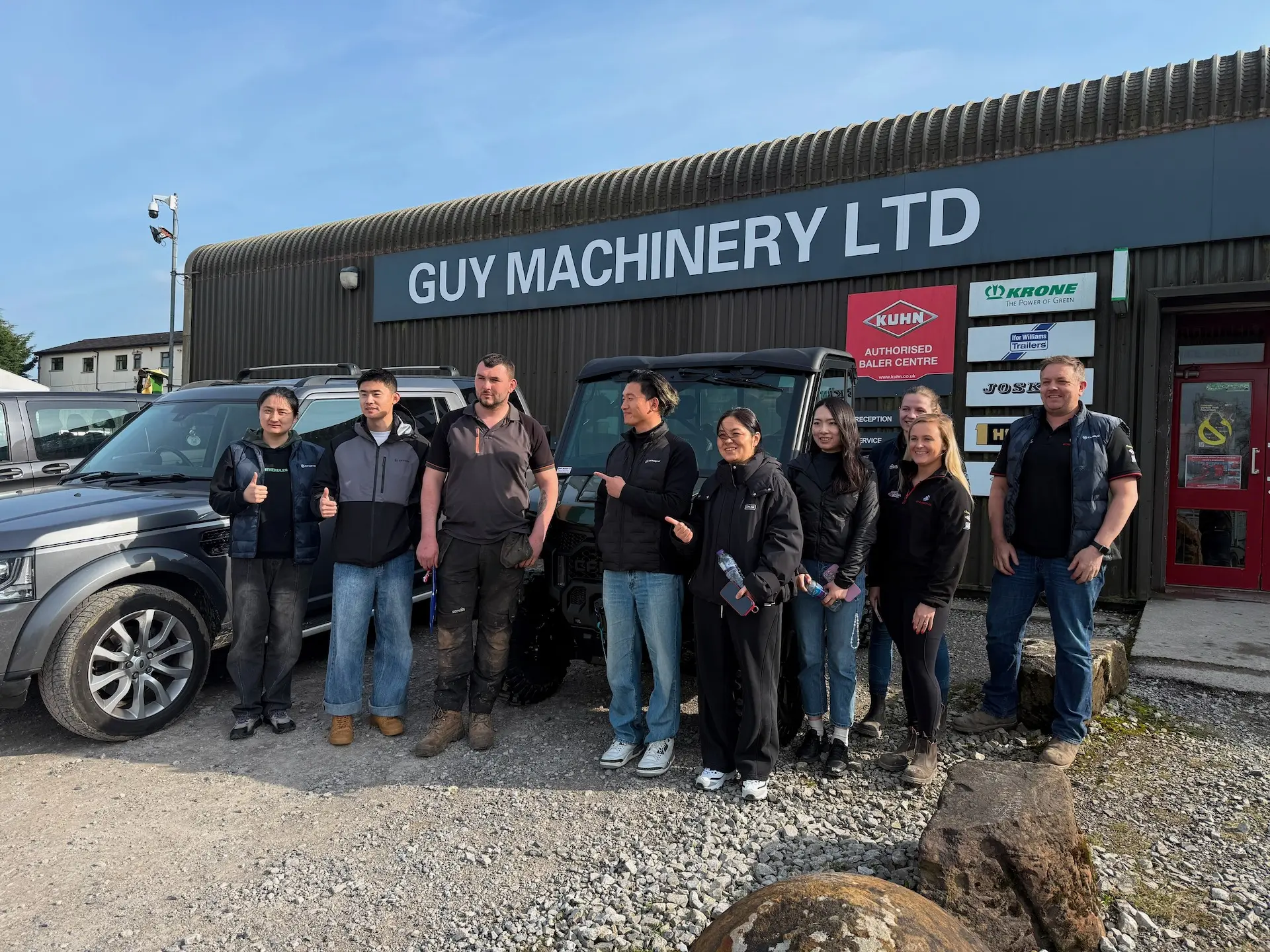 Eight people stand in front of a building labelled "Guy Machinery Ltd," posing next to CFMOTO vehicles and smiling at the camera, showcasing innovative options for UK farmers and agricultural UTVs.