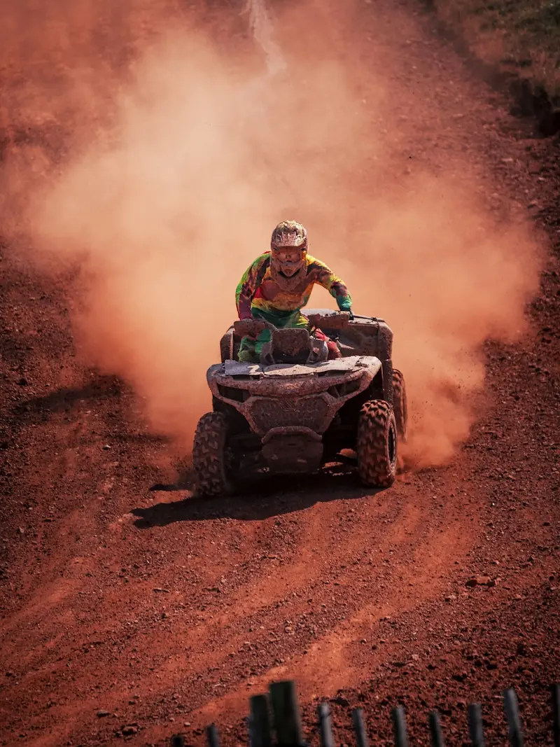 A person wearing a helmet and colorful gear rides a CFMOTO CFORCE 1000 ATV on a dirt track, kicking up a large cloud of dust behind them in the thrilling 4x4 class event.