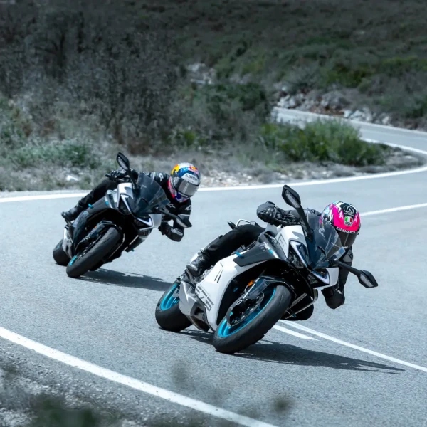 leisure riding motorcycles Two motorcyclists wearing helmets ride sport bikes, leaning into a curve on a paved road surrounded by greenery, enjoying the thrill of leisure riding.